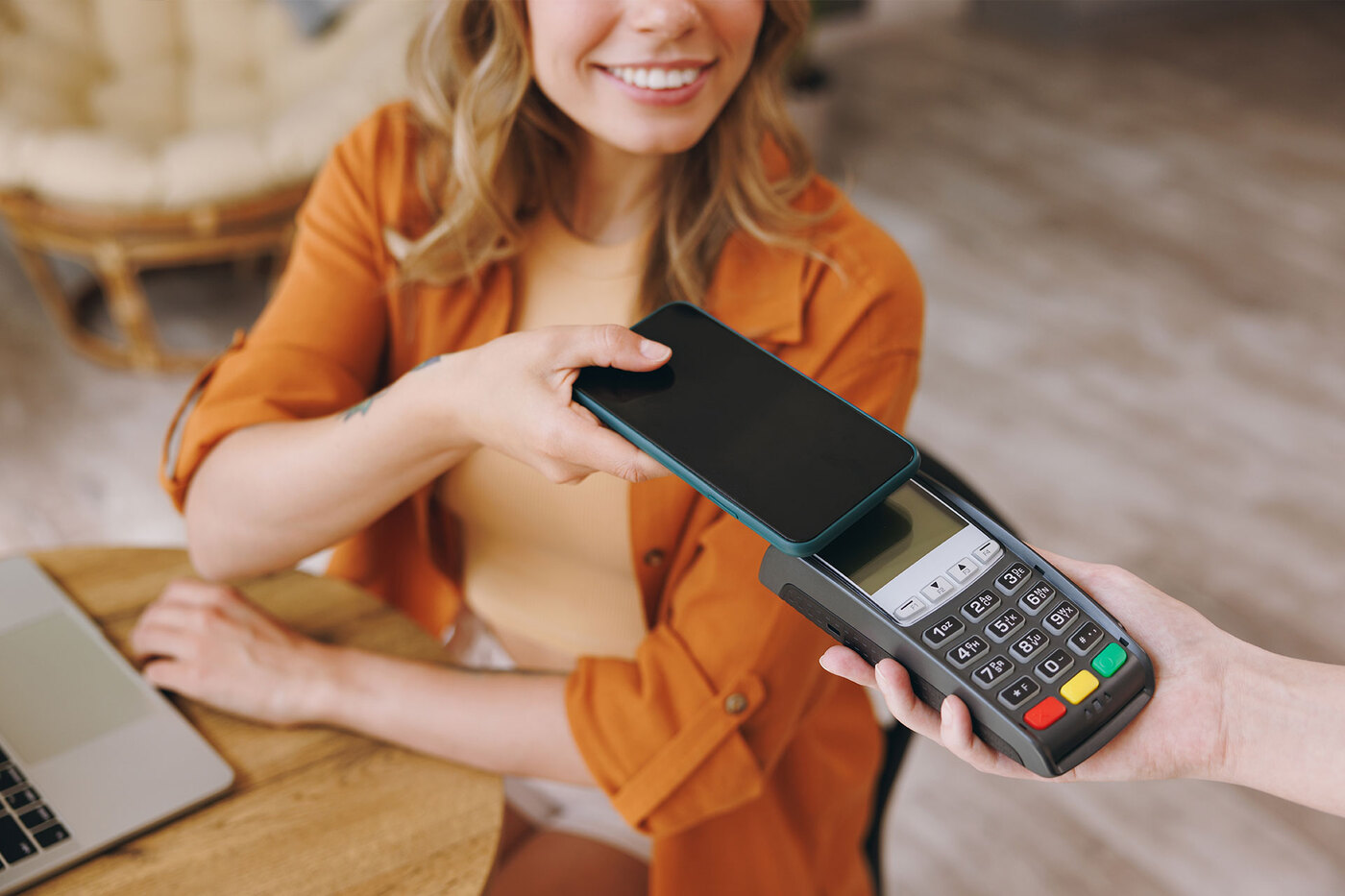 Kobieta przy stoliku płaci telefonem.