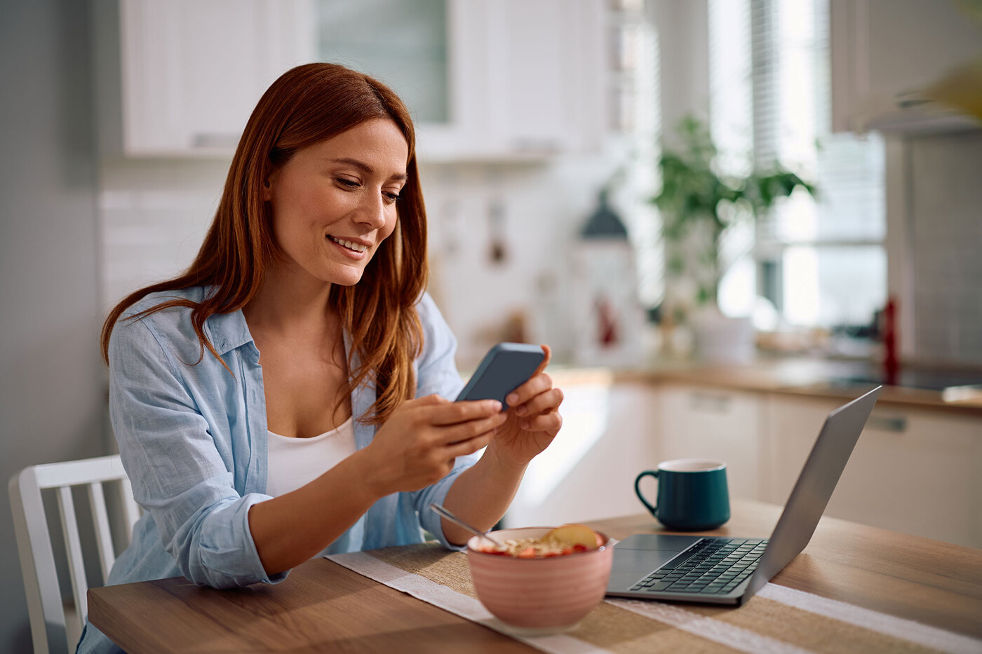 Kobieta przegląda telefon przy stole kuchennym.