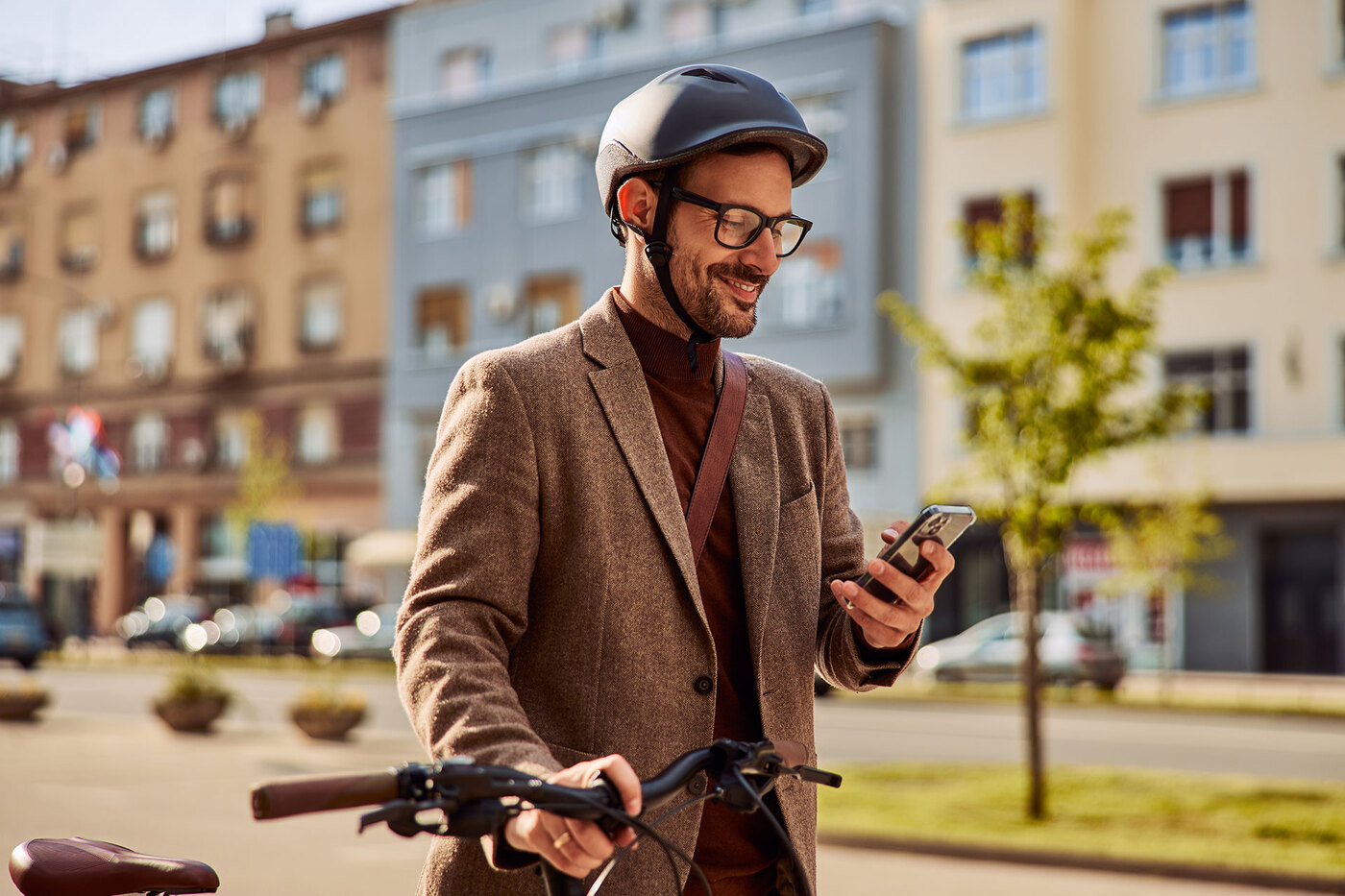 Mężczyzna idąc przez miasto prowadzi rower i patrzy w telefon.