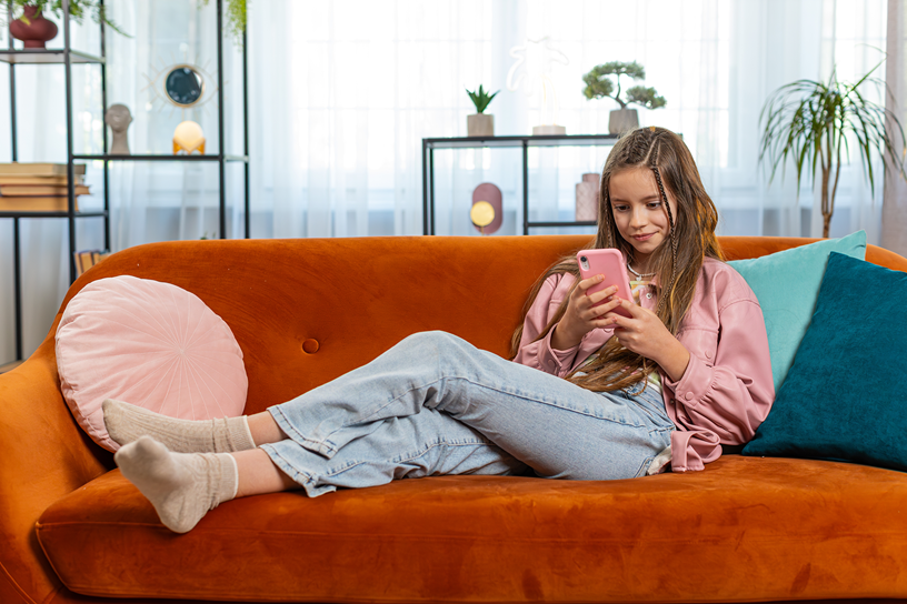 Dziewczyna siedzi na sofie i przegląda telefon.