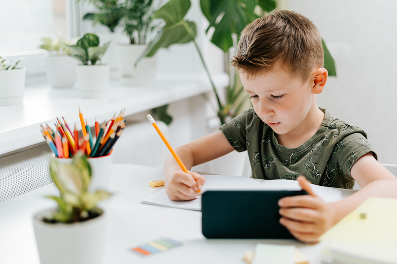 Chłopiec rozwiązuje zadanie i trzyma telefon w ręku.
